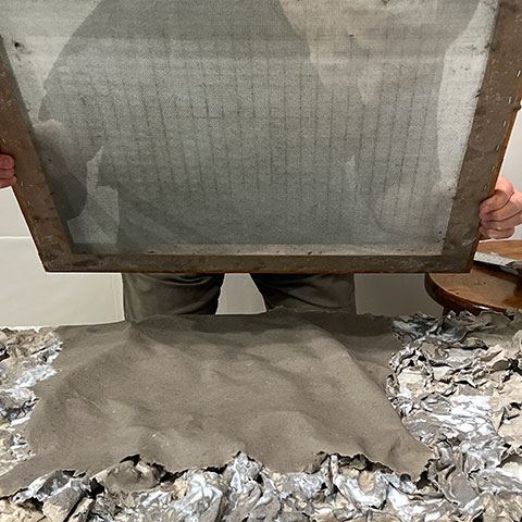 Ruggero Vanni lifting the papermaking screen from the relief mold, the wet pulp sheet visible below beginning to take the three-dimensional form of the cast relief, 2024.
