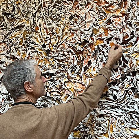 Ruggero Vanni applying final earth pigment accents by hand to the cast relief surface of The Wind Blowing Over the Sea, working close to the material, 2024.
