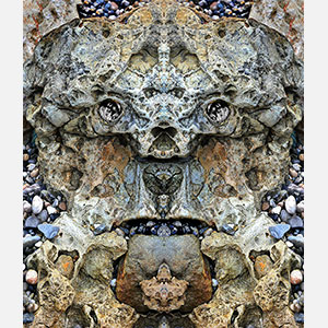 Perceptual fine art photograph by Enzo Ragazzini in which a mosaic rock formation of pebbles and compressed stone yields through mirroring a luminous face lit from within. Mainly cool gray, sandy ochre colors. Title: Creature - Stone VII. Link to the artwork's dedicated page featuring high-resolution detailed images, full info, and an in-depth analysis of its artistic significance.