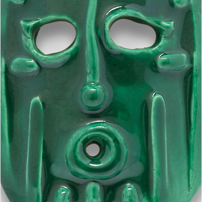 Detail of a figurative ceramic mask sculpture by Giorgio Crisafi, green glaze, shield-shaped with geometric apertures and battlement crown, Masks series. Title: Maschera Zufolo II