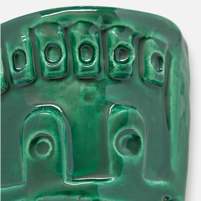 Detail of a figurative ceramic mask sculpture by Giorgio Crisafi, green glaze, shield-shaped with geometric apertures and battlement crown, Masks series. Title: Maschera Zufolo II